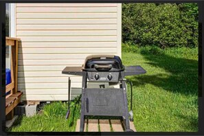 A portable grill set up in a grassy area with a wooden bench and a shed in the background.