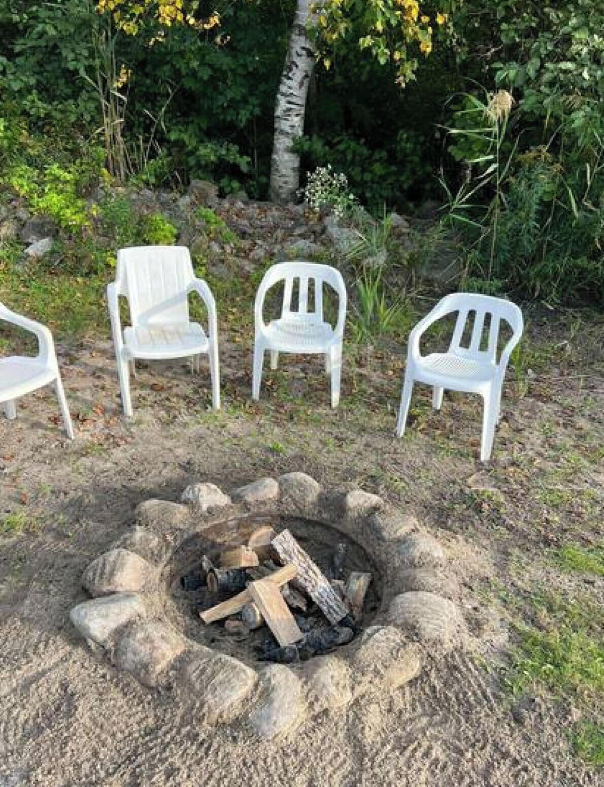 Un foyer avec des bûches, entouré de quatre chaises en plastique blanches.
