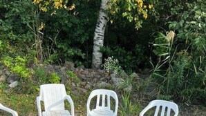 Un brasero con leña, rodeado por tres sillas de plástico blanco.