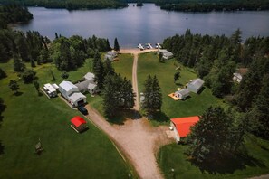An aerial view of a lakeside property with multiple cabins, a central path, and surrounding greenery.