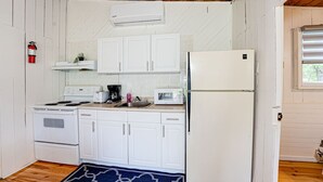 Una cocina compacta con armarios blancos, un refrigerador blanco, un microondas, una estufa y una cafetera.