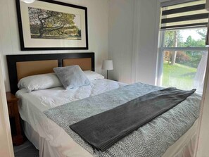 A neatly made bed with a patterned bedspread and pillows, a bedside table with a lamp, and a framed picture on the wall.