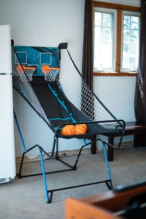 A room with a basketball hoop, a window with curtains, and a refrigerator.