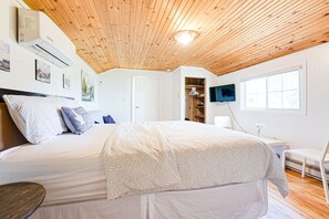 Ein Schlafzimmer mit Holzbalkendecke, einem Bett mit weißer Bettwäsche, einem an der Wand befestigten Fernseher und einem Fenster.