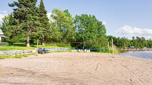 En sandvolleyspillplan med nät, omgiven av träd och en sjö.