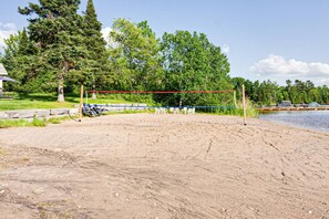 Ein Beachvolleyballfeld aus Sand, mit Netz, umgeben von Bäumen und einem See.