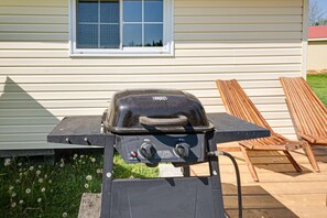 A portable grill on a wooden deck with a house in the background.