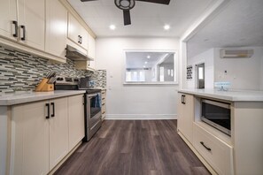 Una cucina moderna con pensili in legno chiaro, zoccolo piastrellato e una finestra che offre luce naturale.