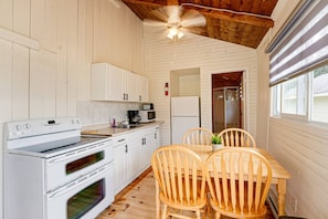A compact kitchen with white cabinetry, a stove, microwave, and a ceiling fan.