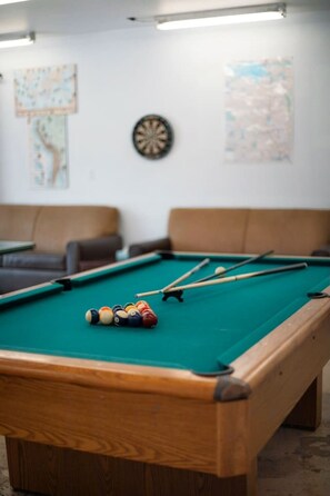 Una mesa de billar con bolas y tacos, un dardo y mapas en la pared.