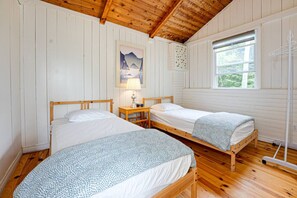 Una habitación con dos camas de madera, una mesita de noche, una lámpara, una ventana y un tendedero fijado a la pared.