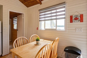 A wooden-paneled room with a table and chairs, a window with blinds, a trash bin, and a sign on the wall.