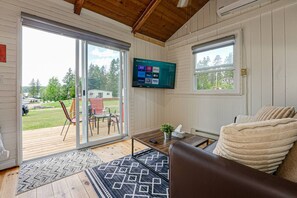 A cozy living room with a large TV, a comfortable couch, and a view of a deck with outdoor furniture.