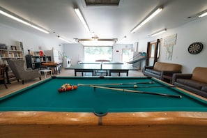 A pool table in a room with a sofa, a bookshelf, and a dartboard.
