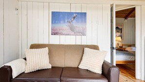 A brown leather sofa with two white pillows, a framed wildlife painting on the wall, and a wooden floor. - Lake Cecebe Retreat #6- Maijac Resort & Marina (Burk`s Falls)