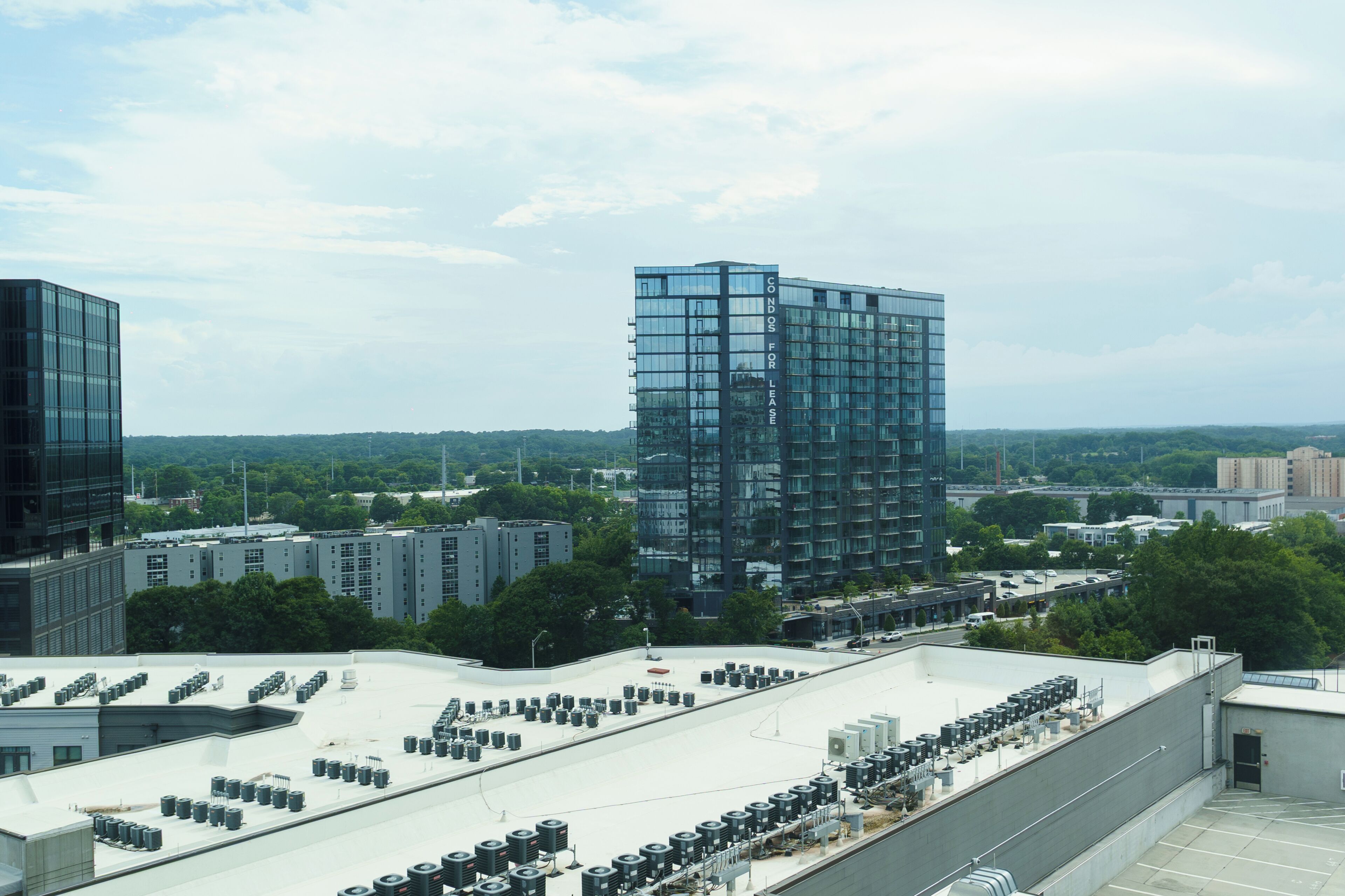 A modern building with a glass facade, surrounded by other structures and greenery.