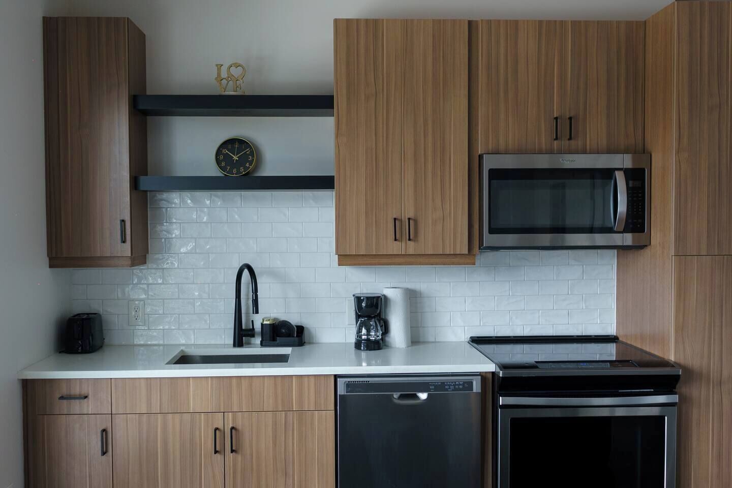 Eine moderne Küche mit Holzausstattung, Mikrowelle aus Edelstahl, Geschirrspüler und einer Kaffeemaschine.