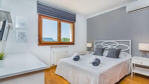 A bedroom with a bed, bedside tables, a radiator, a window, and a desk. - Waterfront Port D'alcudia Villa for 8 (Alcúdia)