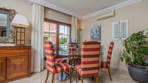 A dining area with a glass table, striped chairs, a potted plant, and artwork on the walls. - Waterfront Port D'alcudia Villa for 8 (Alcúdia)