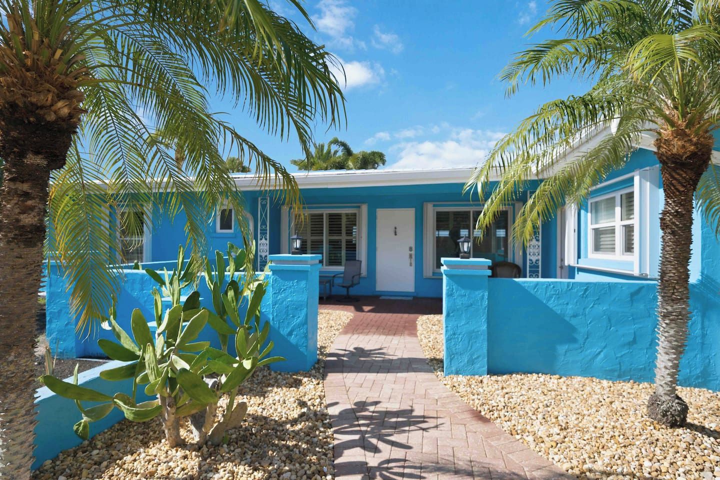 A building with a blue exterior, a paved entrance, and palm trees.