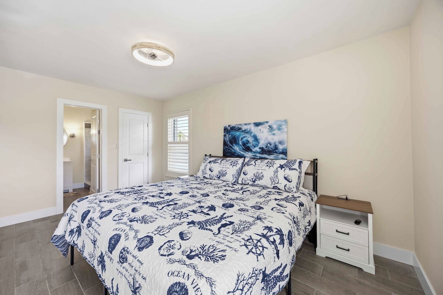 A bedroom with a bed, a nightstand, a wall-mounted painting, and a door leading to another room.