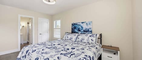 A bedroom with a bed, a nightstand, a wall-mounted painting, and a door leading to another room.