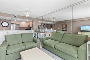 Ein modernes Wohnzimmer mit grünen Sofas, einem weißen Couchtisch und einer Küche im Hintergrund.
