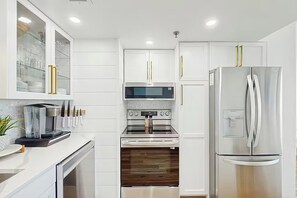 Eine moderne Küche mit weißen Schränken, einem Edelstahl-Kühlschrank, einer Mikrowelle und einer Kaffeemaschine.