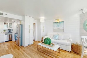 Ett modernt vardagsrum med en vit soffa, ett soffbord och ett kök i bakgrunden.