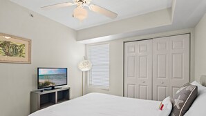 Ein Schlafzimmer mit einem Bett, einem Fernseher, einem Deckenventilator und einer Tür.