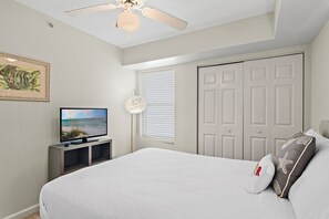 A bedroom with a bed, a television, a ceiling fan, and a door. - Gulf View| Private Beach| Pelican Terrace 1503 (Destin)