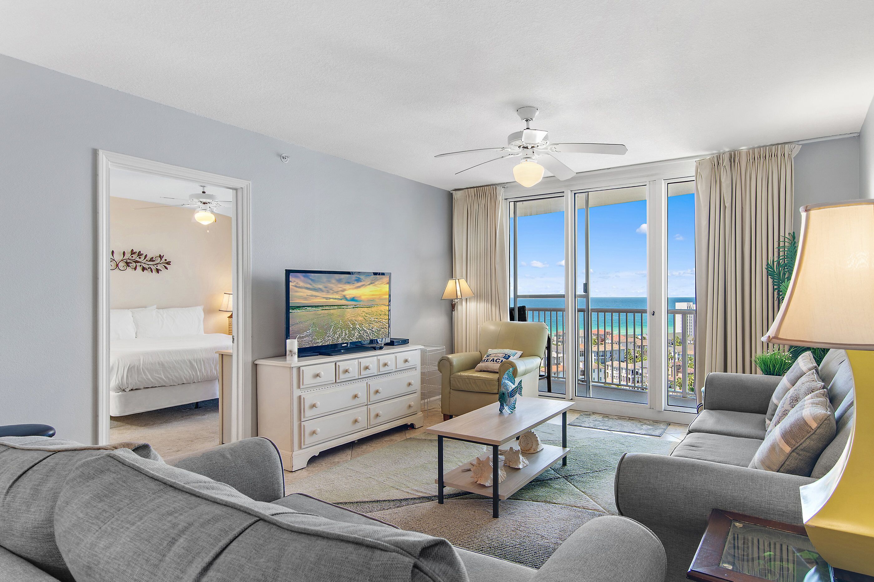 Ein Hotelzimmer mit Bett, Fernseher, Sofa, Couchtisch und einem Balkon mit Meerblick.