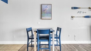 A dining area with a table and chairs, a painting of a bird, and two paddles on the wall. - 🏖️Gulf Views-5 Pools-Laketown Wharf 1817🏖️ (Panama City Beach)