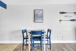 A dining area with a table and chairs, a painting of a bird, and two paddles on the wall. - 🏖️Gulf Views-5 Pools-Laketown Wharf 1817🏖️ (Panama City Beach)