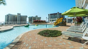A swimming pool area with lounge chairs and umbrellas, surrounded by buildings. - 🏖️Gulf Views-5 Pools-Laketown Wharf 1817🏖️ (Panama City Beach)