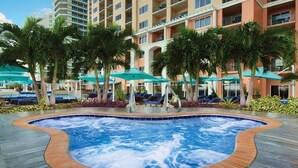 Zona de piscina de hotel con jacuzzi, sillas de descanso y sombrillas.