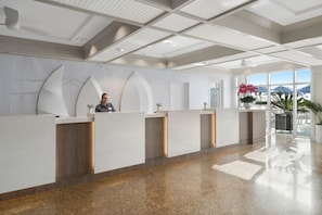A reception area with a modern design, featuring a long reception desk, a ceiling with recessed lighting, and a view of the outdoors through large windows. - Dream Florida Escape in Fort Lauderdale! (Fort Lauderdale)