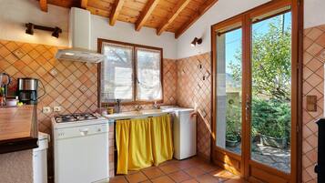 Una cocina con estufa a gas, horno empotrado, cafetera y ventana con cortinas de encaje.