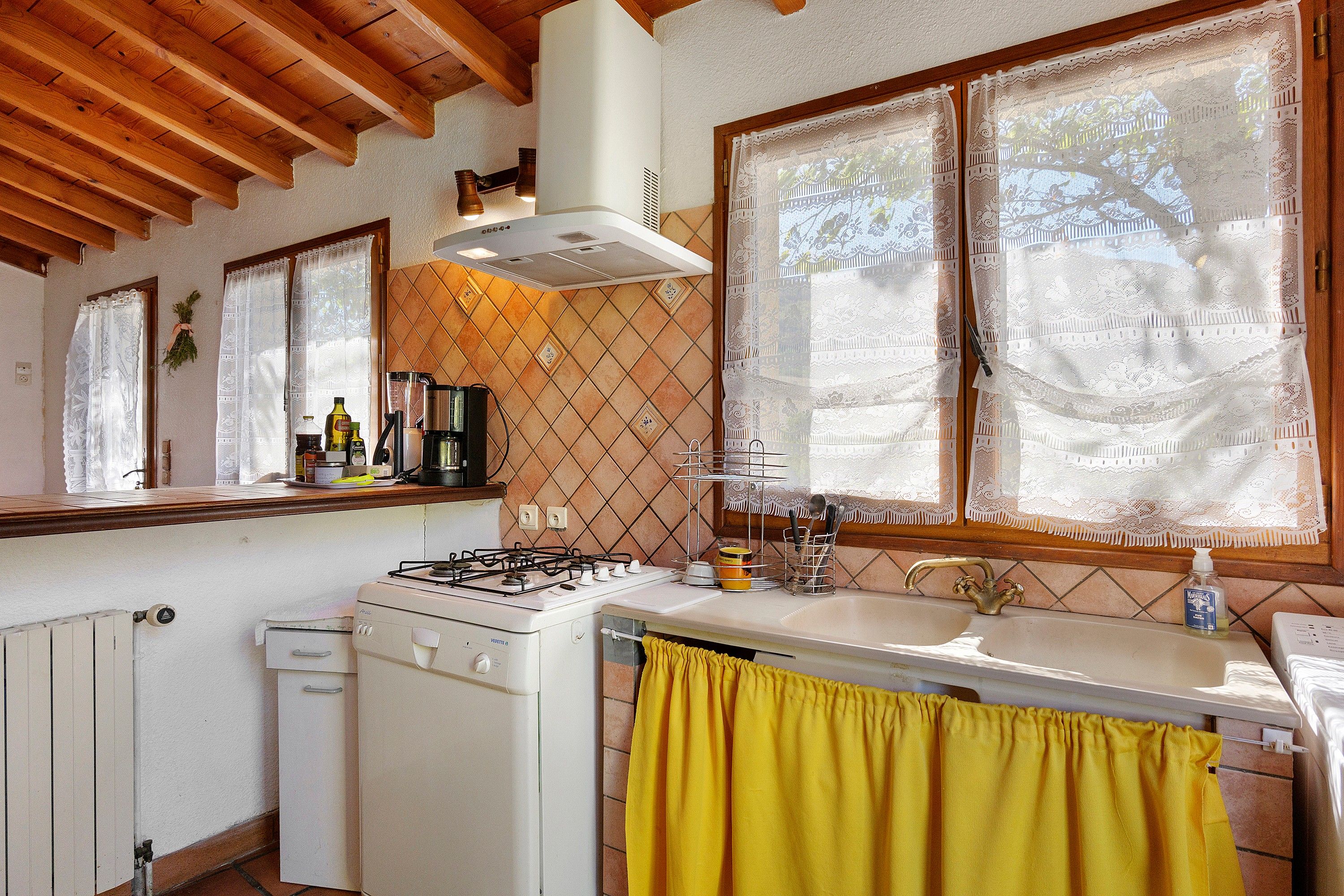 A kitchen with a gas stove, a sink, and a window with lace curtains.