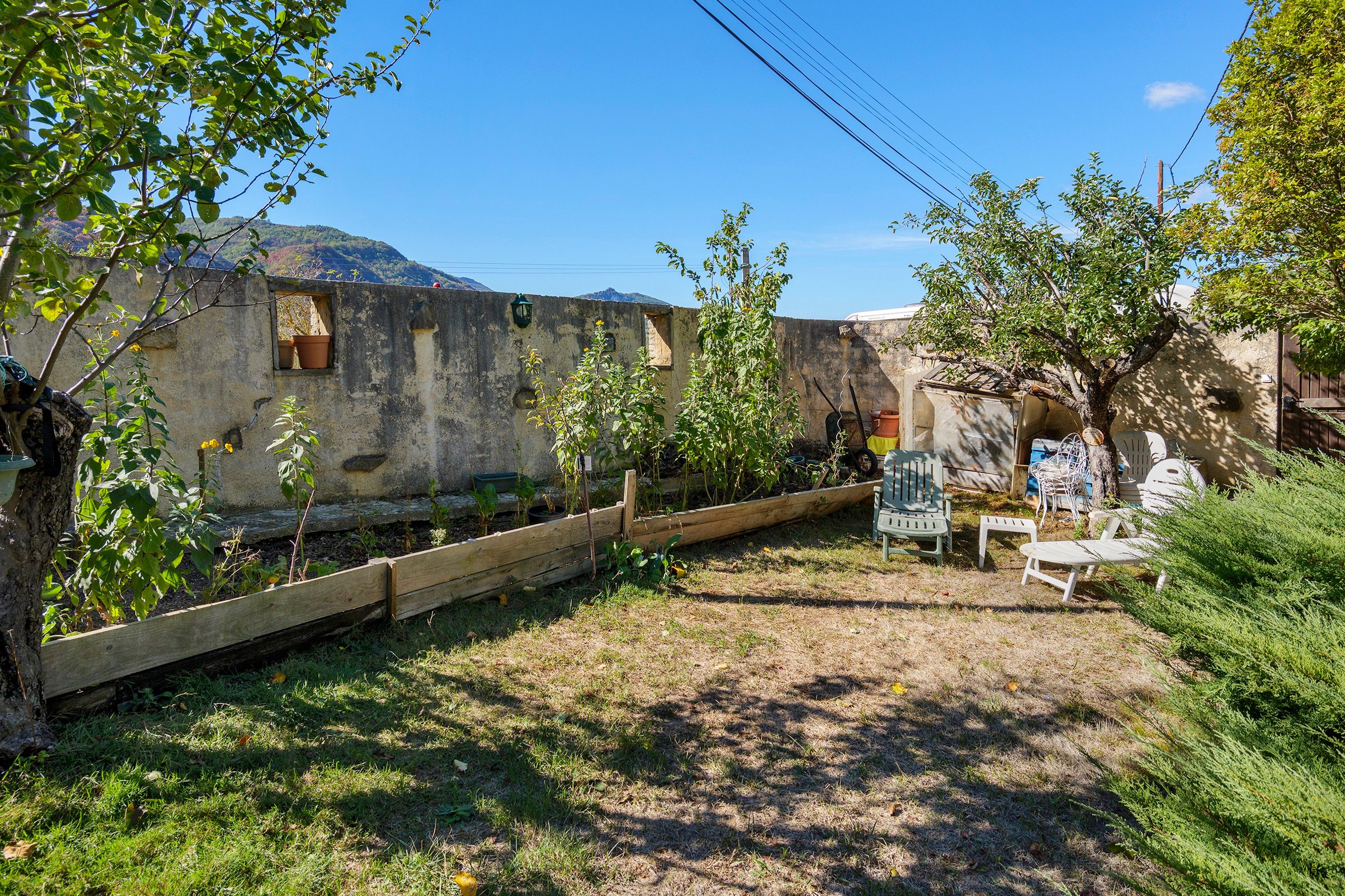 Un jardín con cerca de madera, una mesa con sillas y vistas a una montaña.