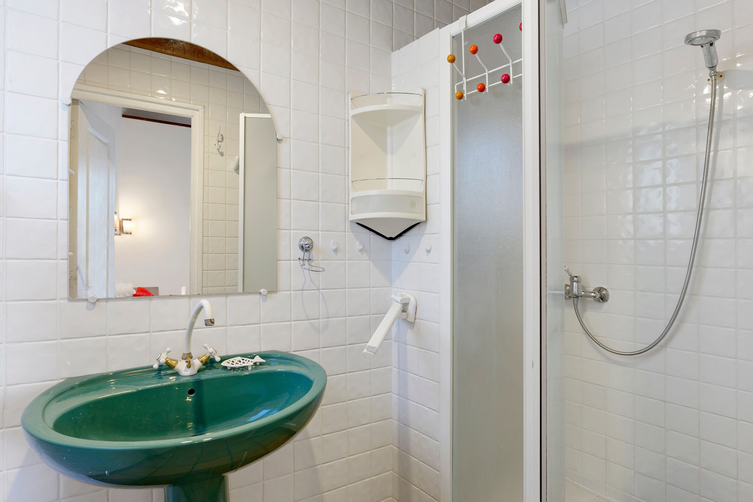 A bathroom with a green sink, a mirror, a shower with a handheld showerhead, and a towel rack.