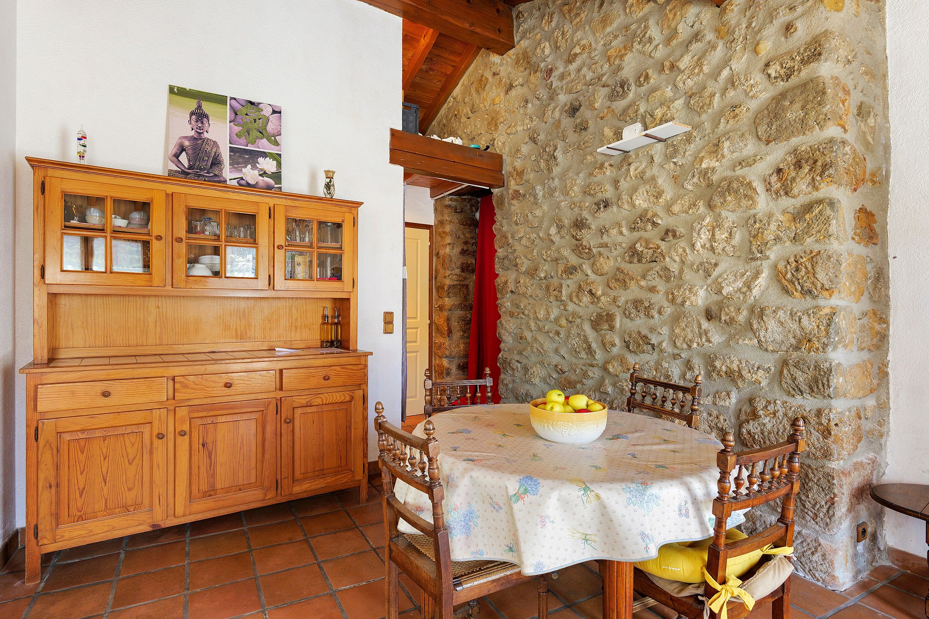 Un comedor rústico con pared de piedra, mobiliario de madera y una mesa con mantel floral.