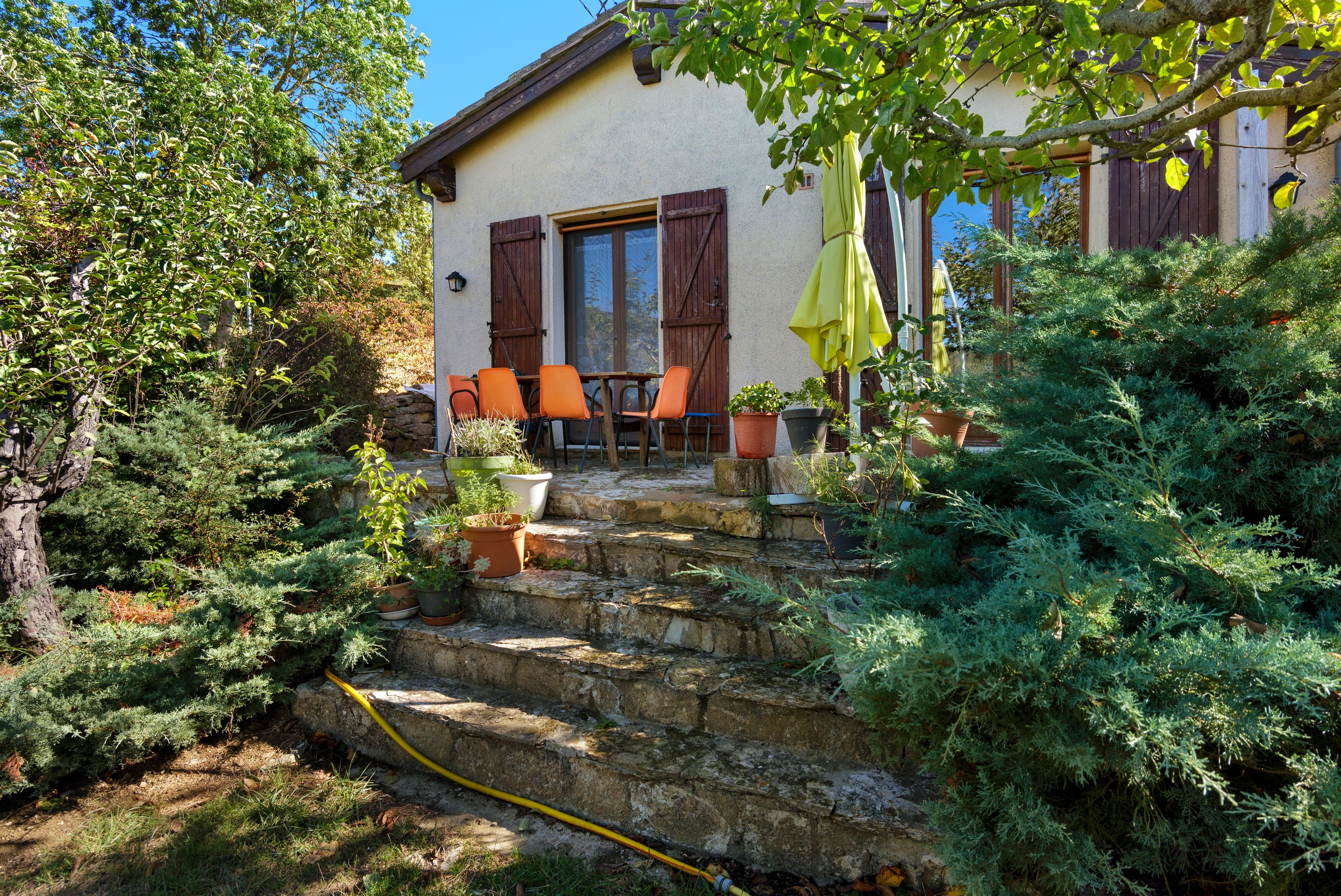 Une maison avec un escalier en pierre menant à un patio aménagé avec des meubles d’extérieur et des plantes en pot.