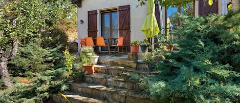 A house with a stone staircase leading to a patio with outdoor furniture and potted plants.