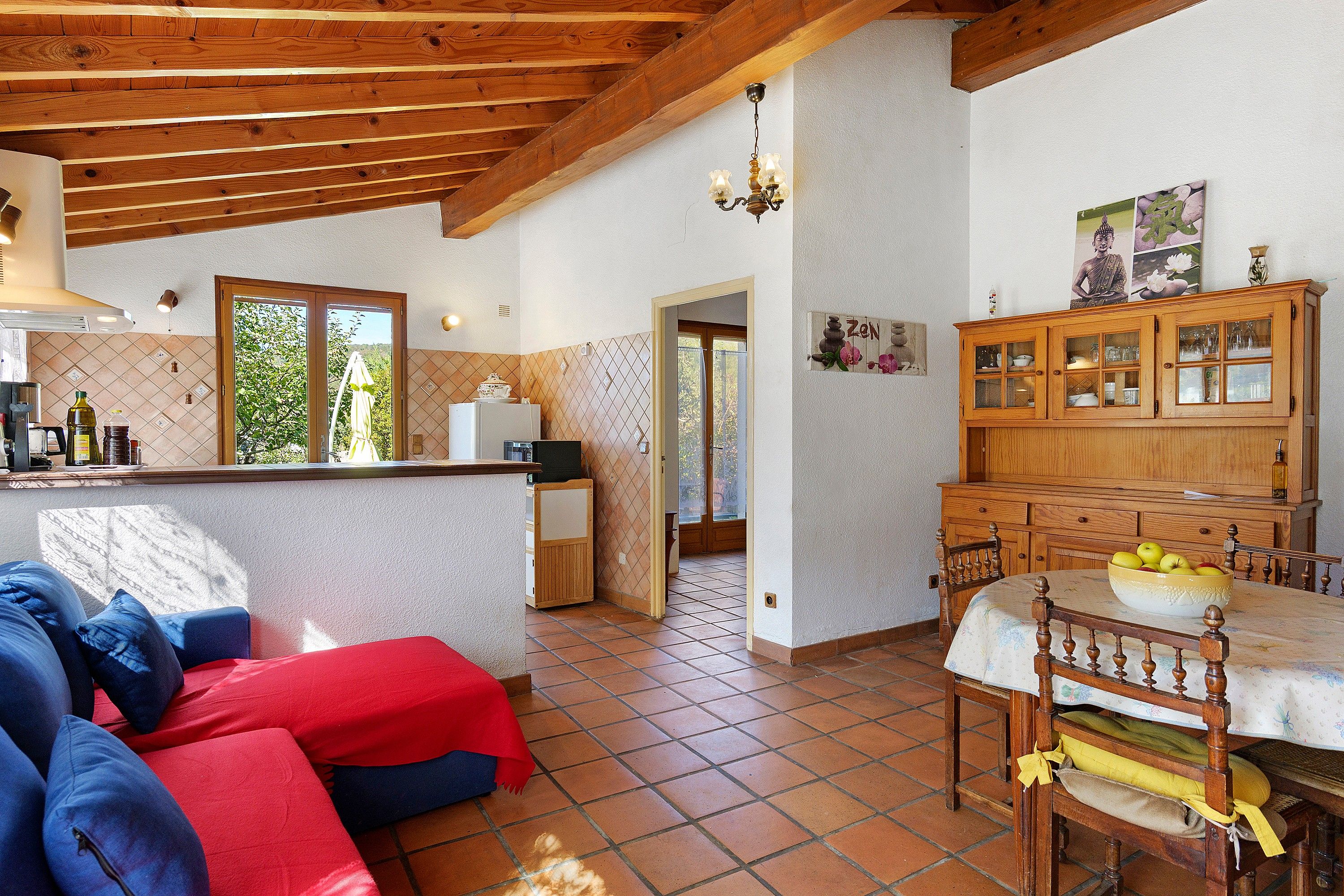 Una sala de estar acogedora con un sofá, una mesa de comedor con un cuenco de fruta y una zona de cocina con un refrigerador y una ventana.