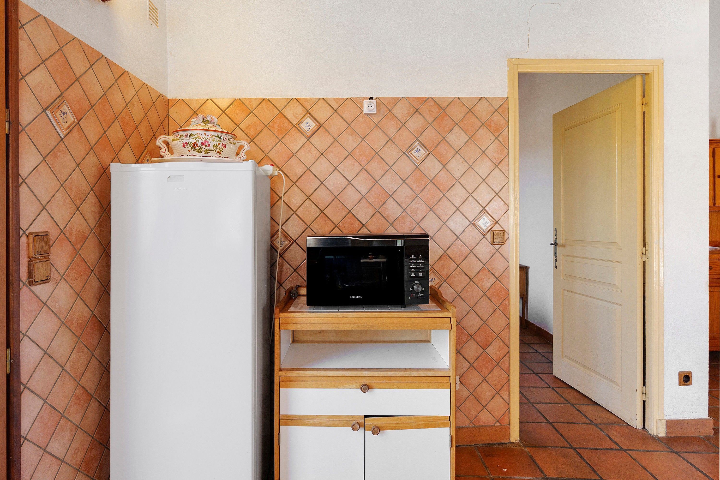 Une cuisine compacte avec un réfrigérateur blanc, un four à micro-ondes posé sur un meuble en bois et un pare-feu en carreaux.