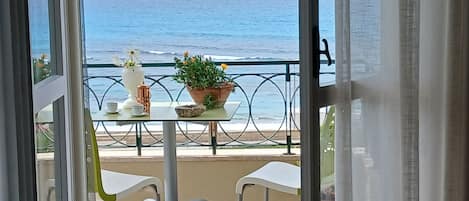 Un balcón con vista al mar, una mesa con sillas y una planta en maceta.