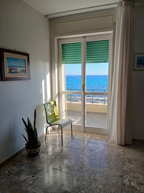 A room with a view of the sea through a sliding glass door, a chair, a potted plant, and a framed picture on the wall. - Spacious beachfront vacation home "LA TERRAZZA SUL MARE DI GALLIPOLI" 3274407527 (Gallipoli)