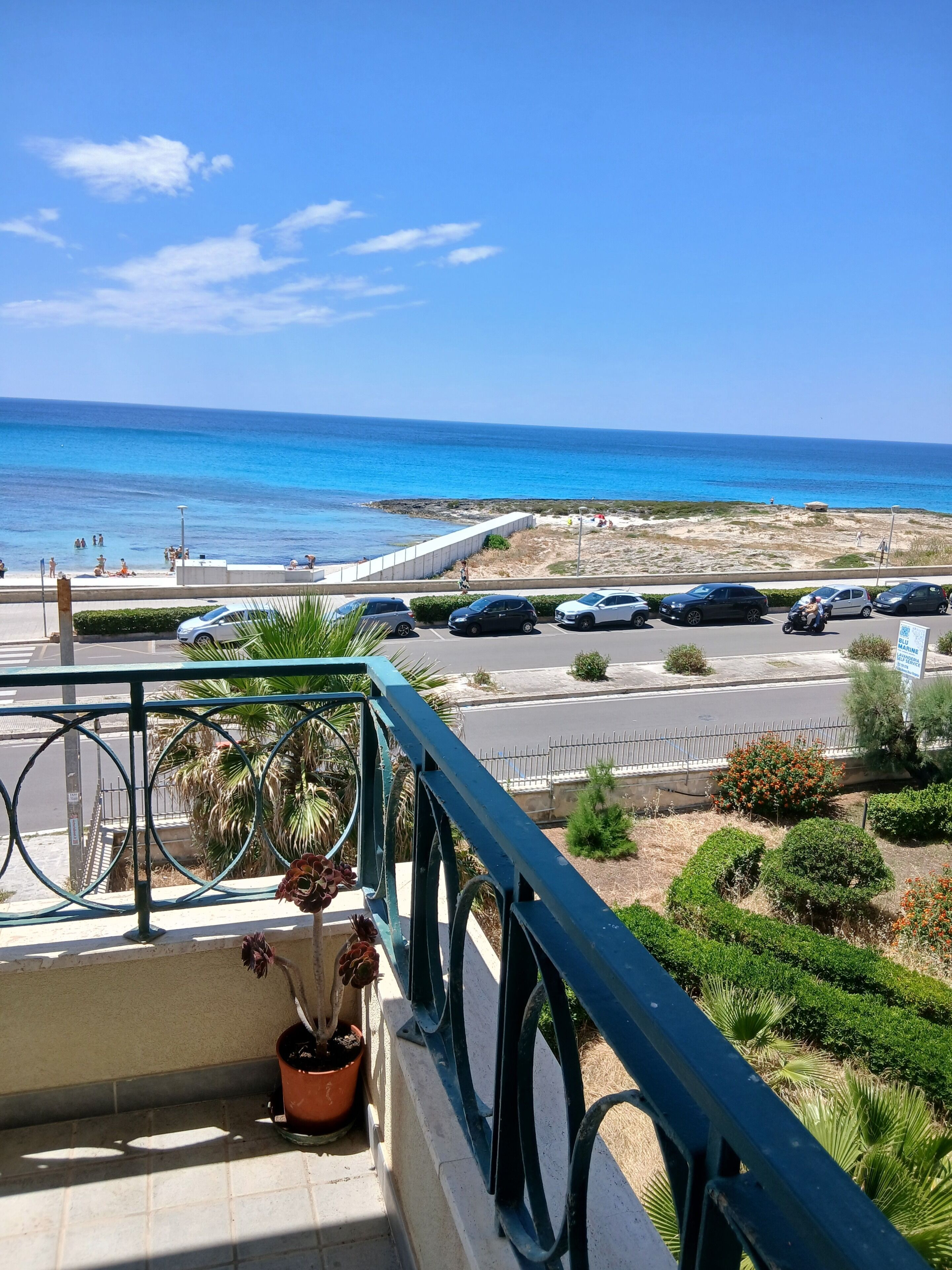 A balcony with a view of the sea, a parking area, and a signboard.