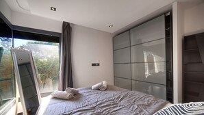 A modern bedroom with a large bed, a mirror, and a view of greenery outside. - Exceptional 9-Bedroom Villa in Mougins (Mougins)